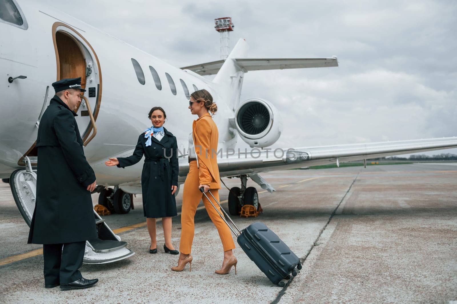 A young woman in yellow clothes is accompanied by an airline workers.