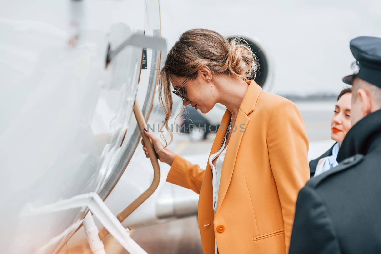 A young woman in yellow clothes is accompanied by an airline workers.