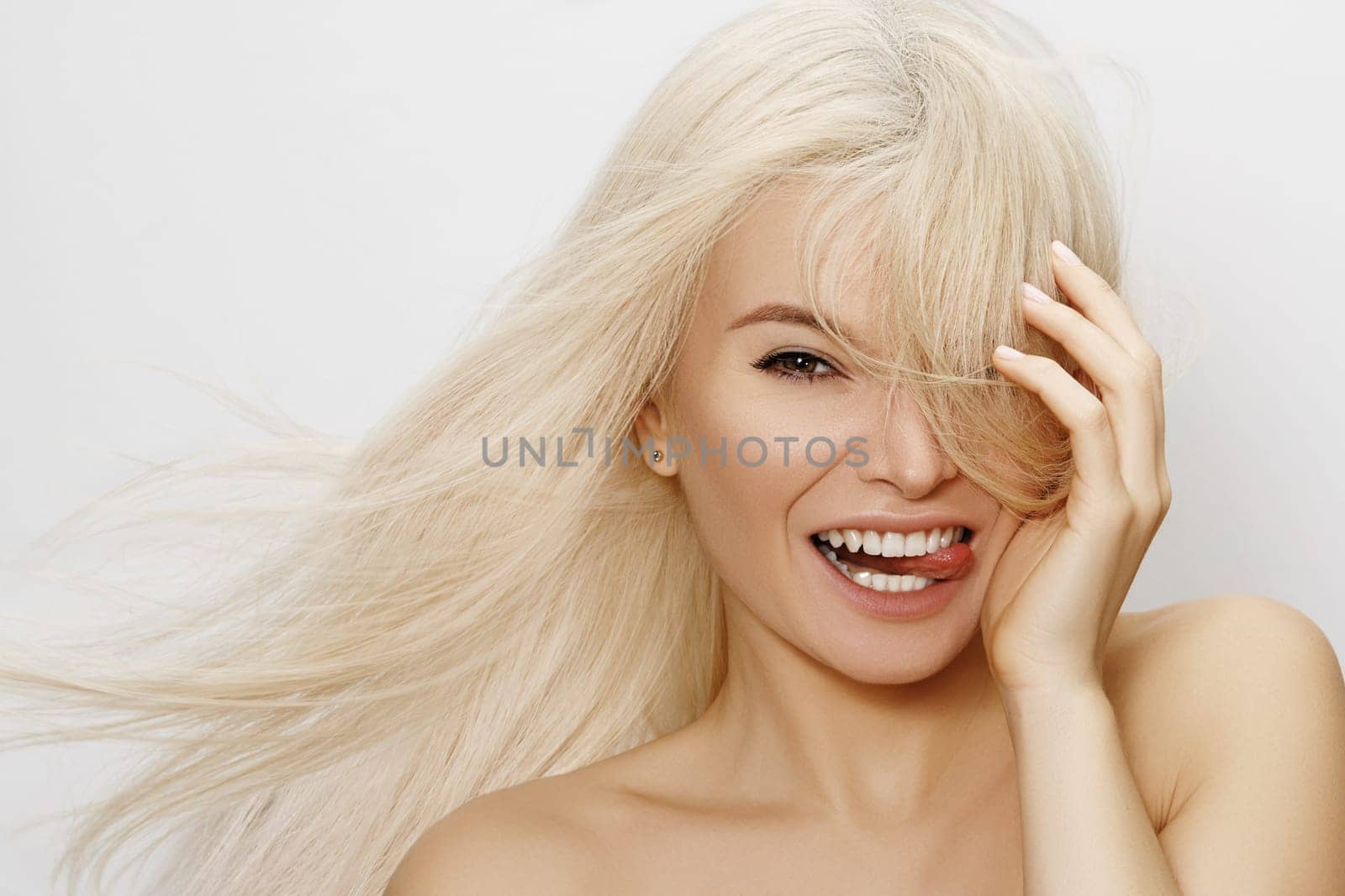 Beautiful woman with magnificent blond hair. Happy model face with windswept flying hair. Shiny long health hairstyle. Beauty and haircare