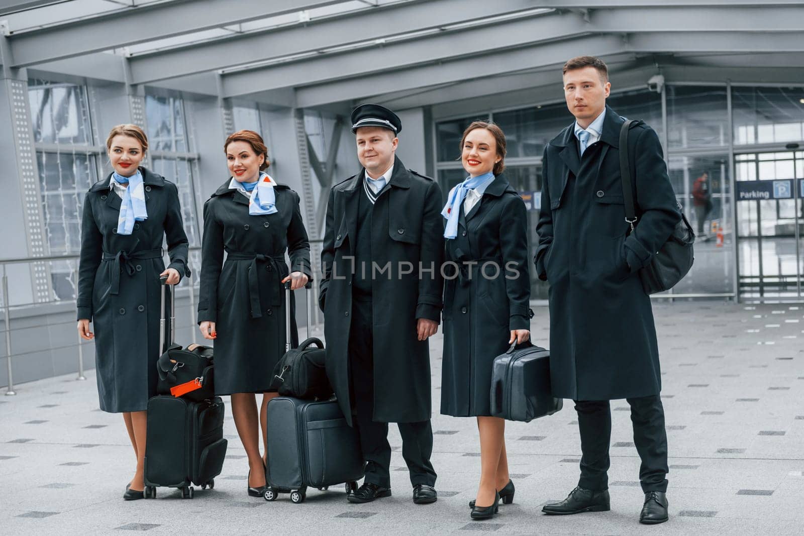 Aircraft crew in work uniform is together outdoors in the airport.