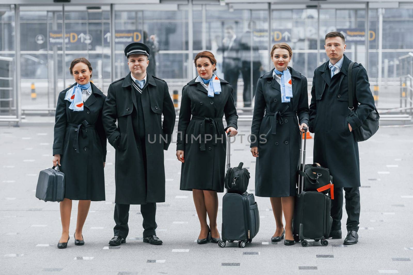 Aircraft crew in work uniform is together outdoors in the airport by Standret