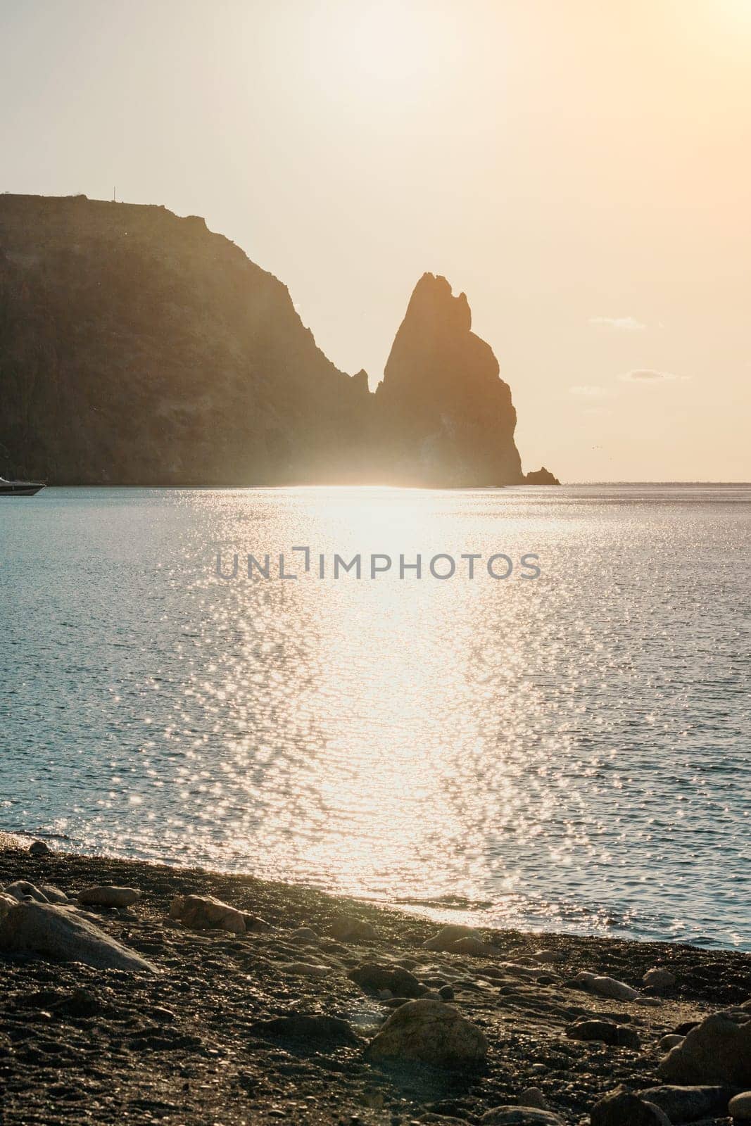 A red burning sunset over the sea with rocky volcanic cliff. Abstract nature summer ocean sea background. Small waves on golden warm water surface with bokeh lights from sun. by panophotograph