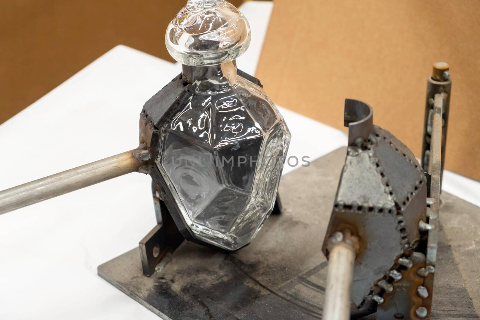 Stylish glass bottle in open metal form on workbench in light workshop at traditional glassblowing plant extreme close view