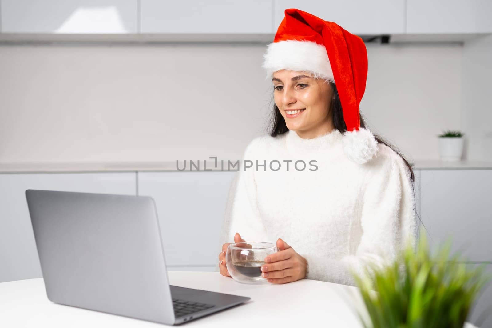 Happy woman with a coffee cup has a meeting online before Christmas. Freelance girl working at home office.