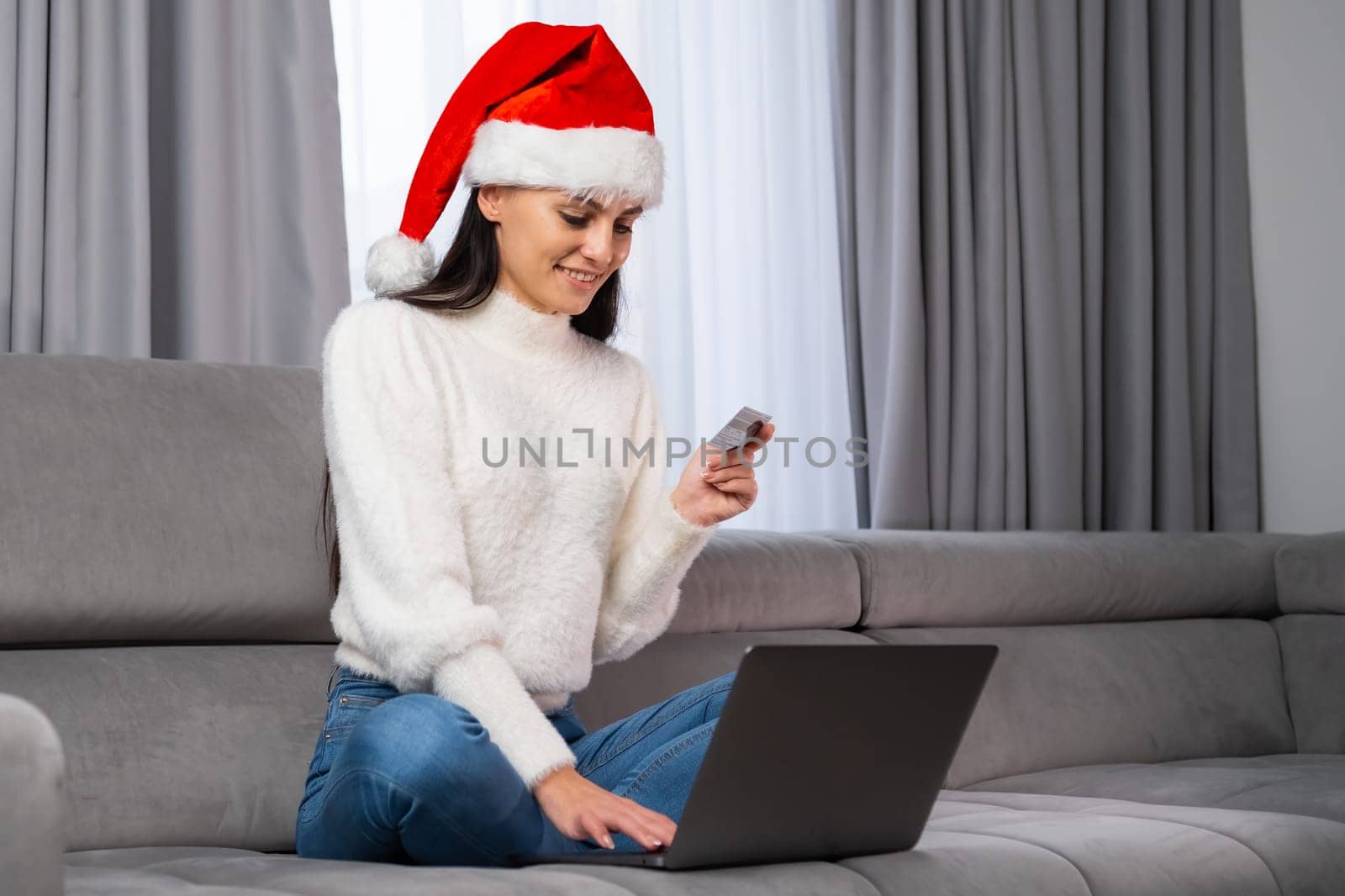 Happy woman wearing a Santa Claus hat using a credit card for paying gifts for Christmas online in the living room.