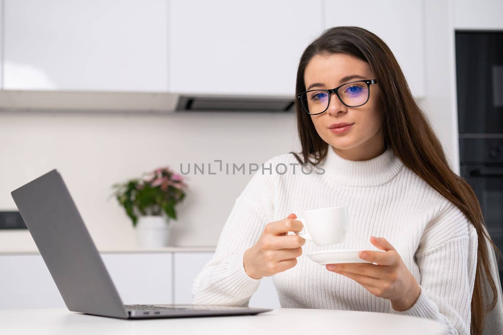 Portrait of young woman in glasses sitting at a desk and holding a cup of coffee in the modern interior. Journalist has a break at the work.