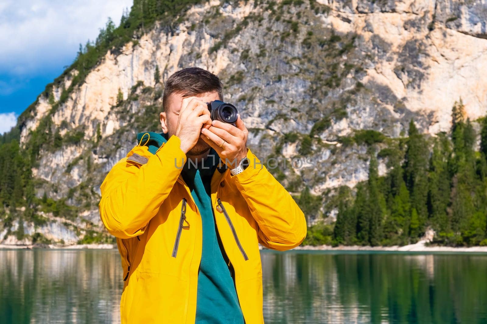 Portrait of the photographer covering her face with the camera on the background of Lake Braies and the Dolomites