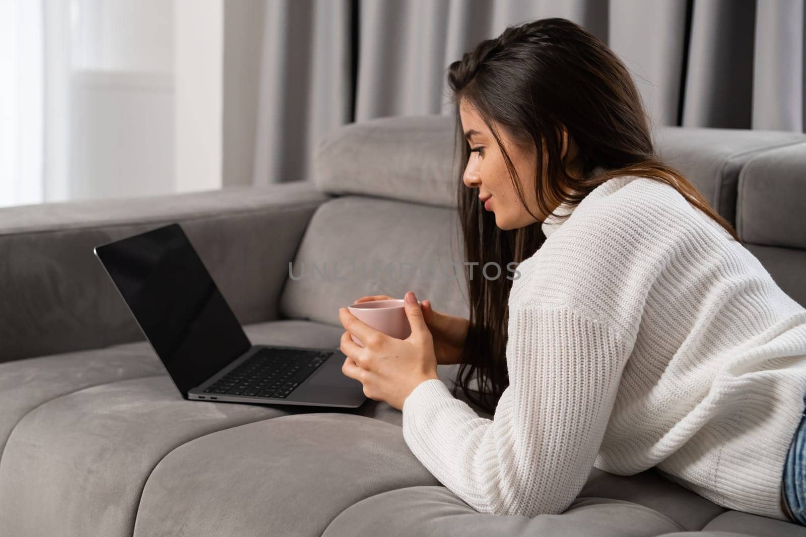 Relaxed pretty young woman laying on the sofa and watching film in a cozy home