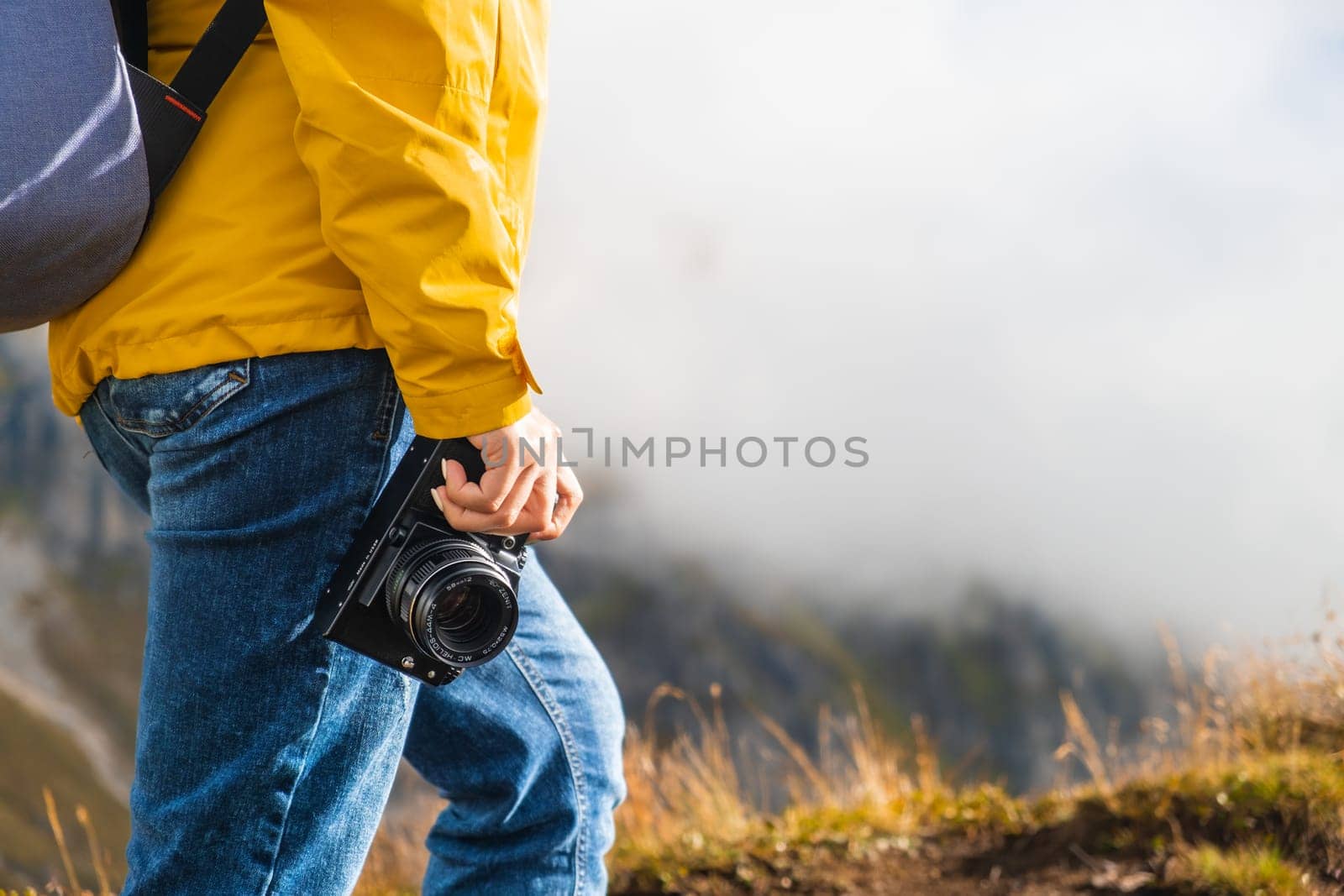 Legs of hiking woman standing and holding a retro camera on the peak of the mountain covered by clouds. Travel concept.
