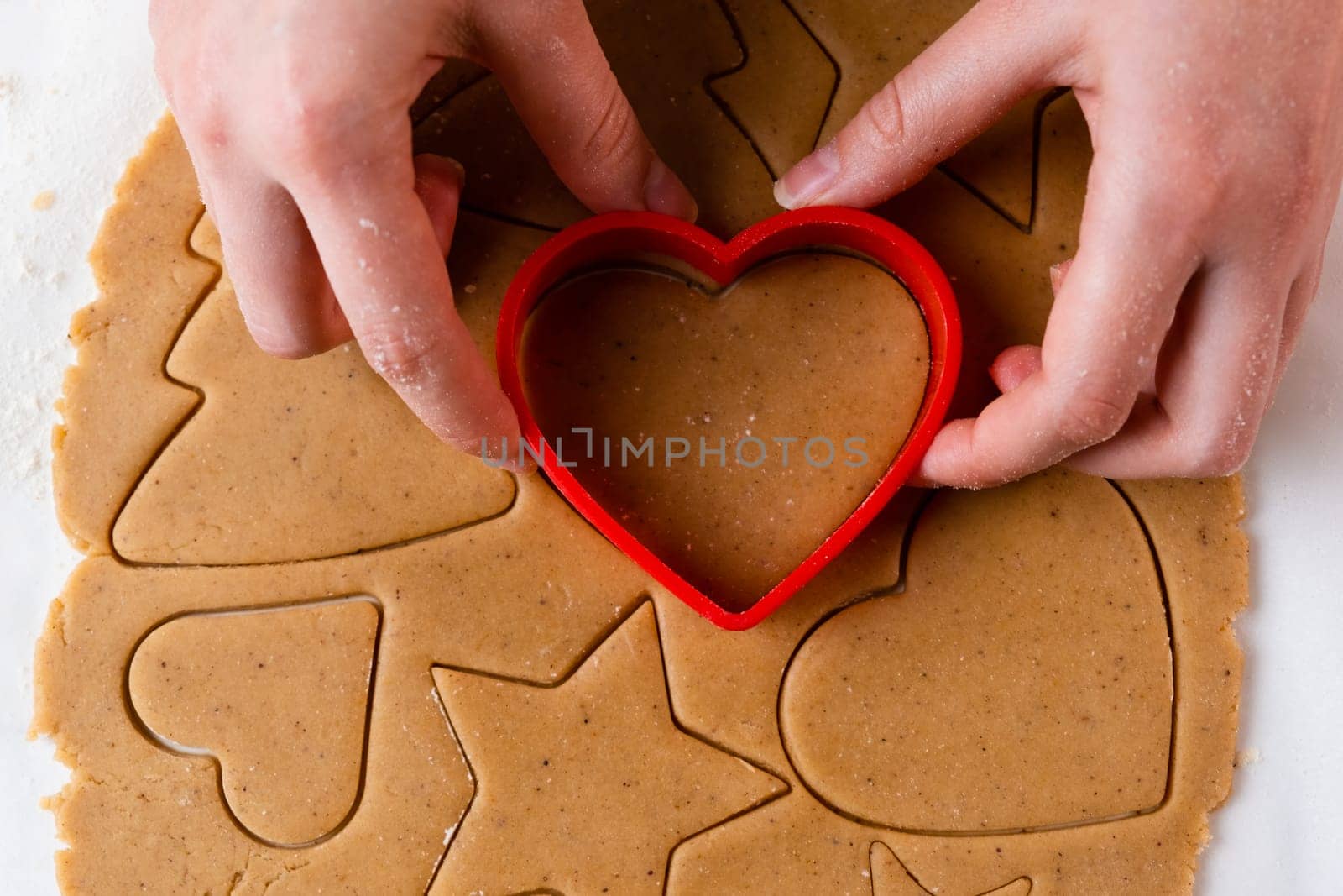 Close up woman making cookies in the shape of heart using plastic baking form for St Valentines Day by vladimka