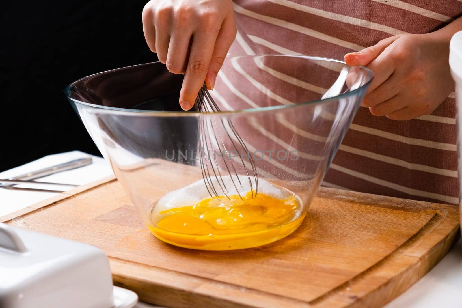 Close up of a womans hands whipping eggs for making dough on the wooden desk in the kitchen. Homemade cooking.