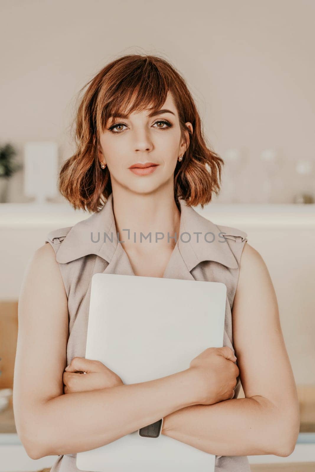 Brunette macbook. Portrait of a woman, she holds a mabuk in her hands and looks at the camera, wearing a beige dress on a beige background
