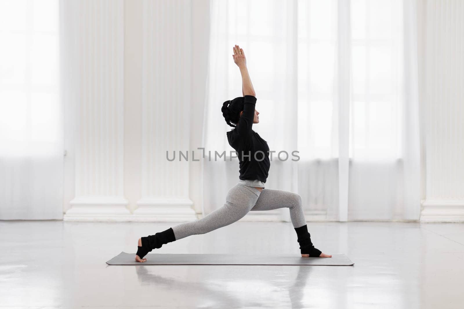 Slim mixed race female yoga lover does virabhadrasana on mat on the floor in her spacious living room. Concept of strengthens the muscles of the legs, tones the knees and ankles by apavlin