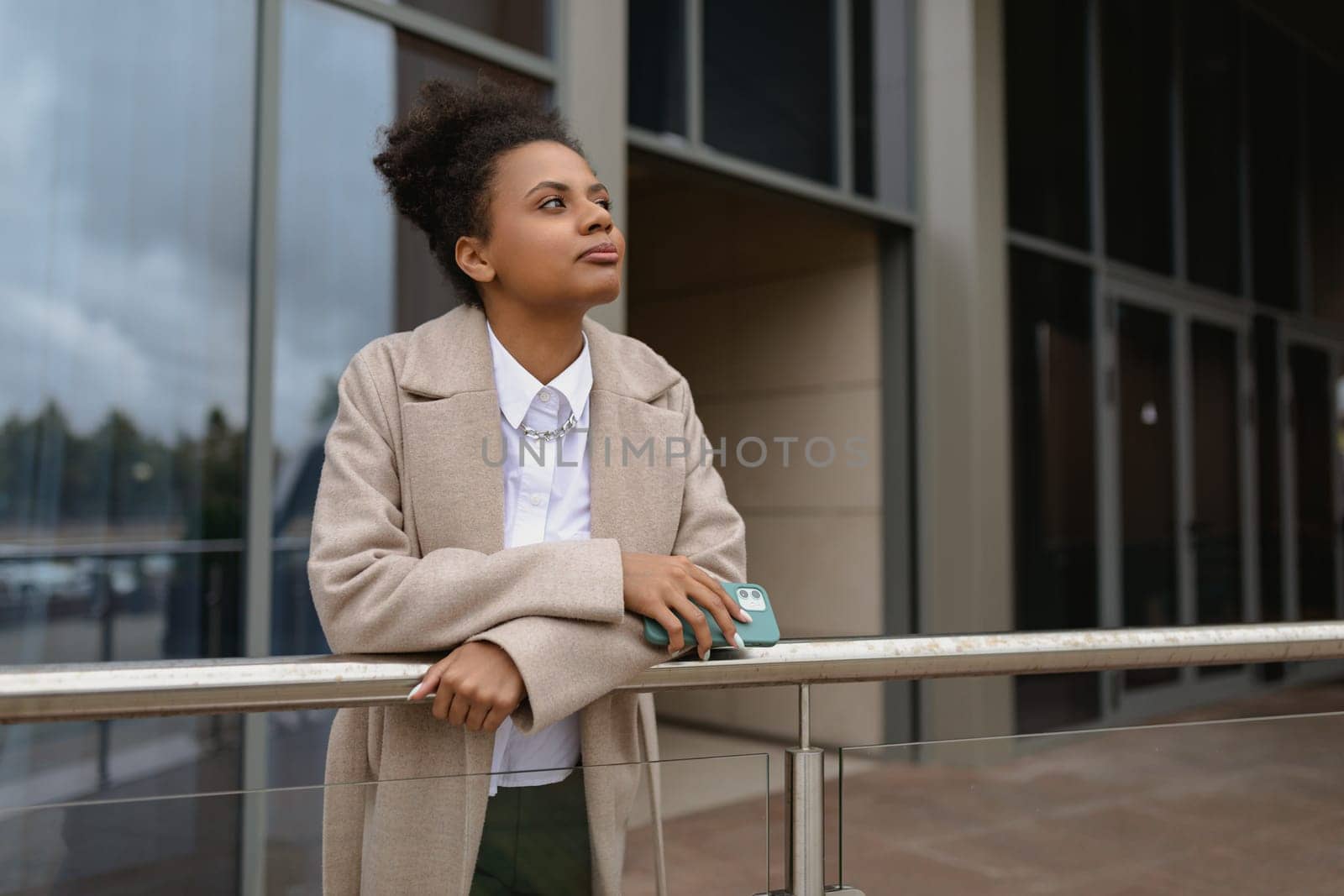 American young woman designer stands thoughtfully in front of a glass business center.