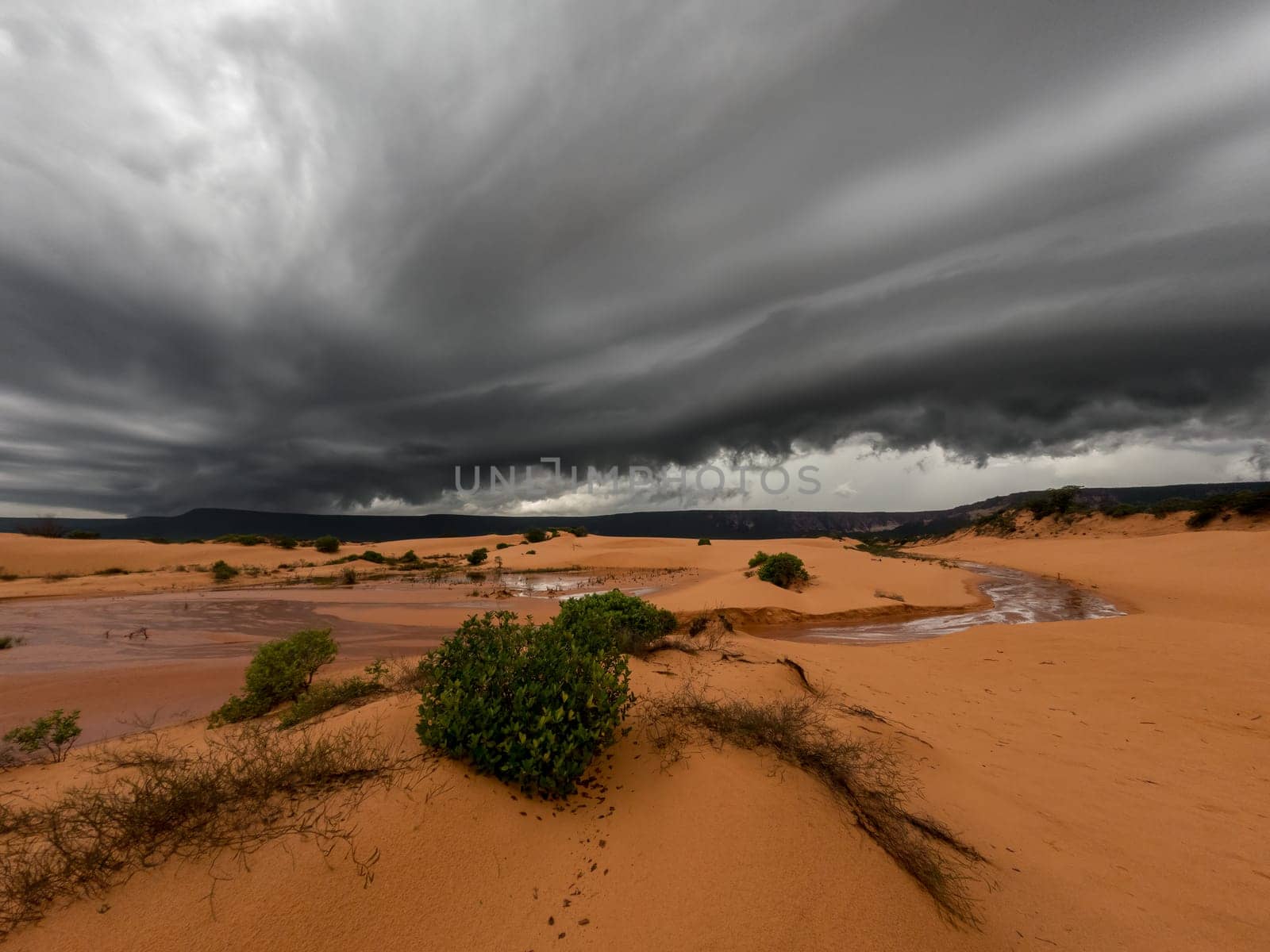 A massive tropical storm approaches the Jalapao sand dunes, creating an impressive and dramatic scene with dark clouds and a stunning sunset.