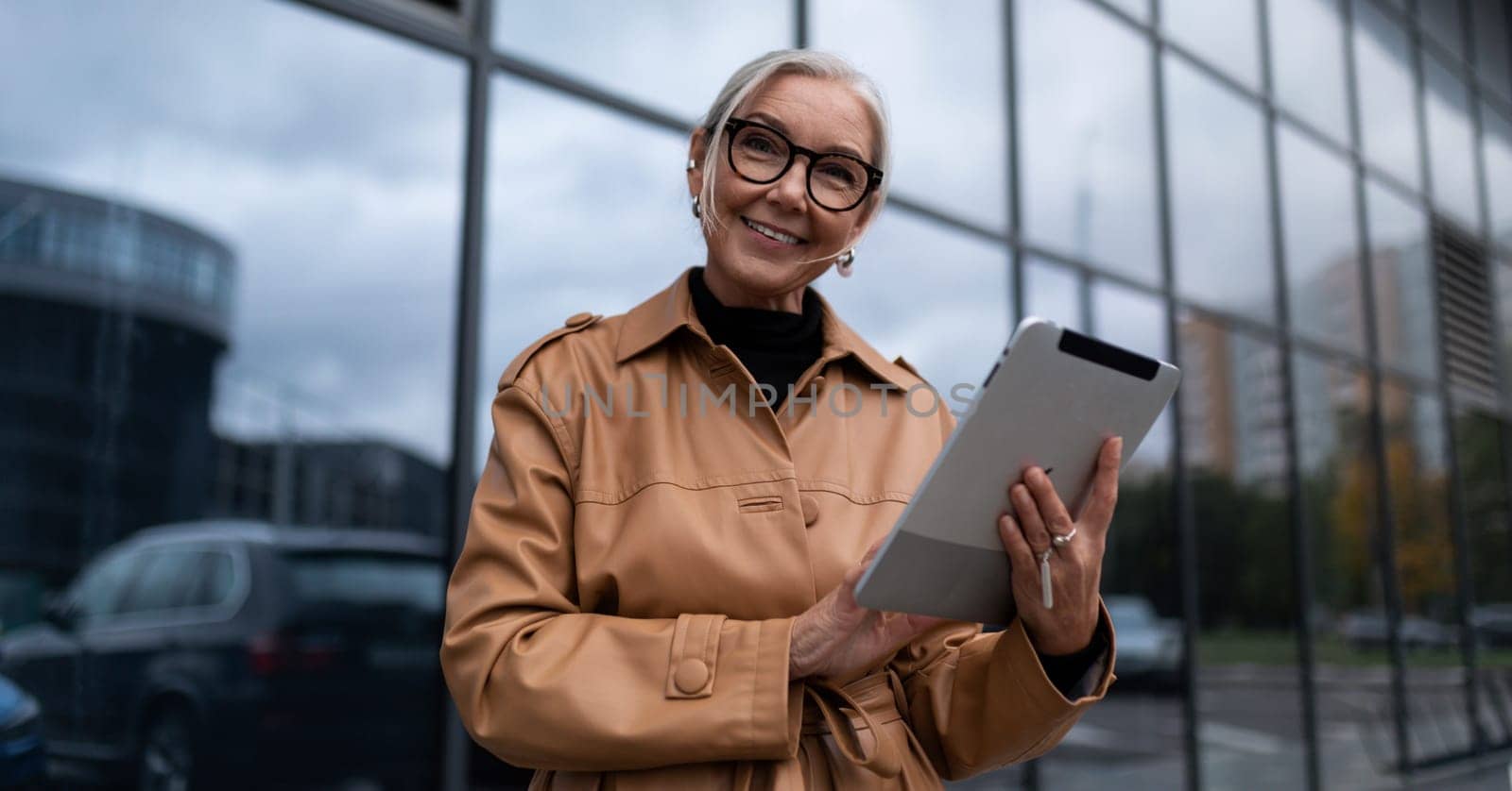 elderly stylish woman with a tablet on the background of a business center, woman leader in business concept by TRMK