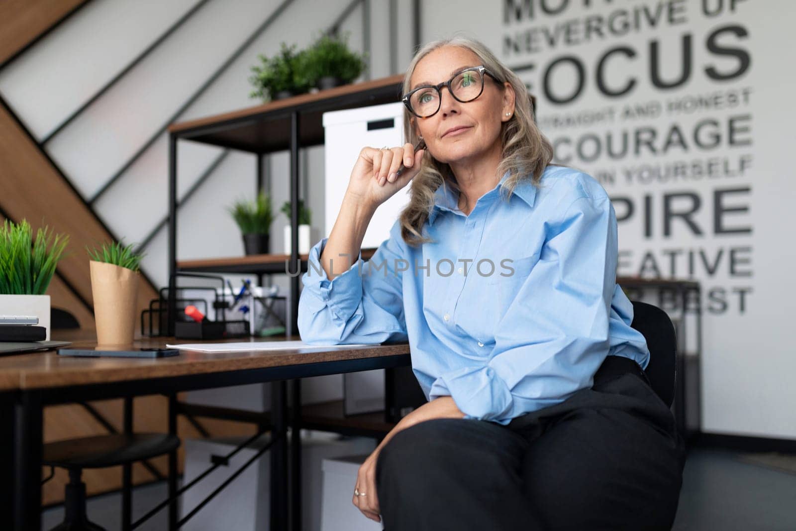 Business woman in the office at the table looks thoughtfully into the distance.