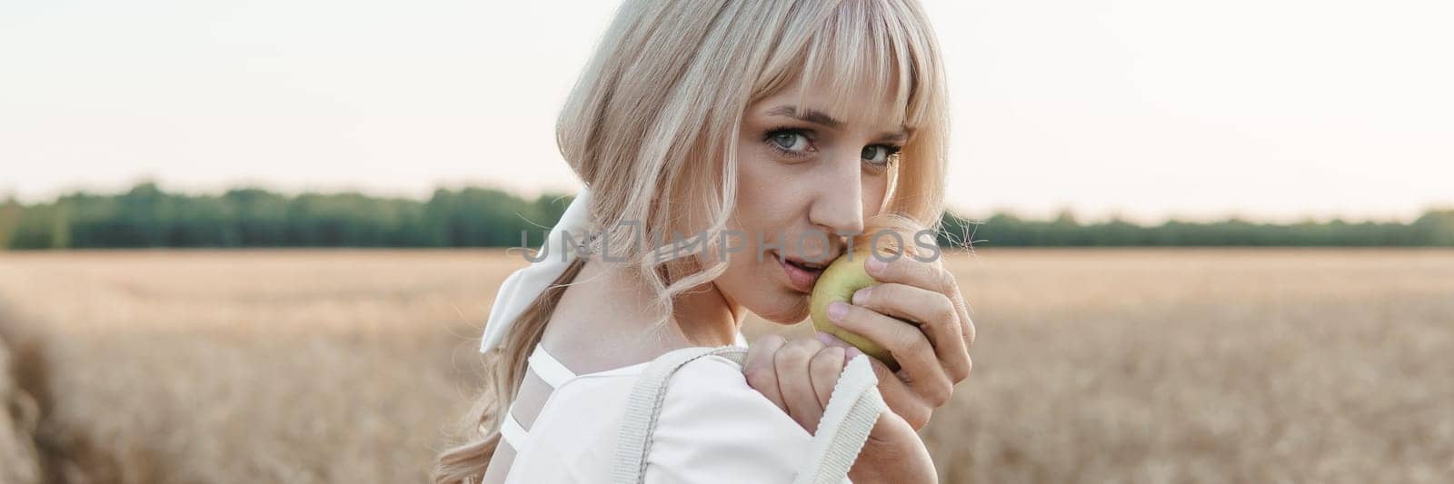 A blonde woman in a long white dress walks in a wheat field. The concept of a wedding and walking in nature.