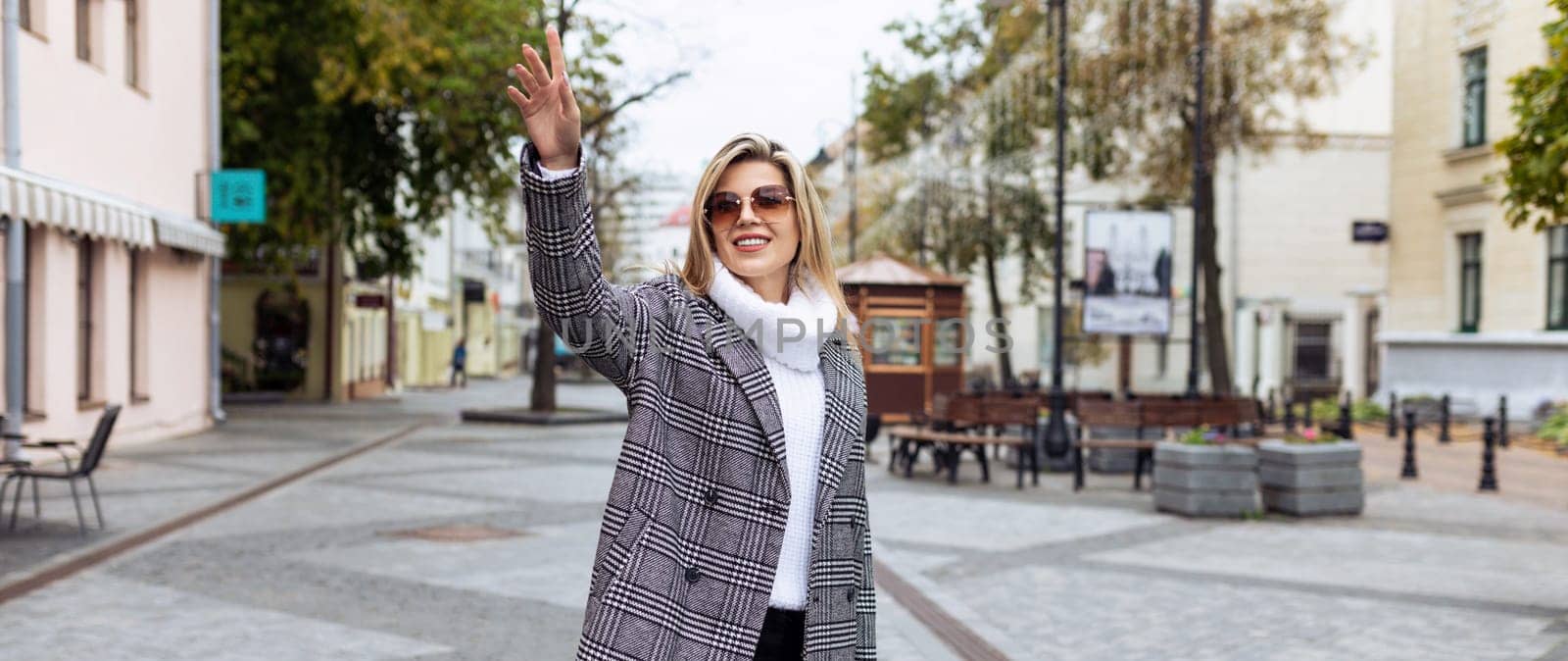 a woman in an autumn coat catches a taxi with her hand up by TRMK