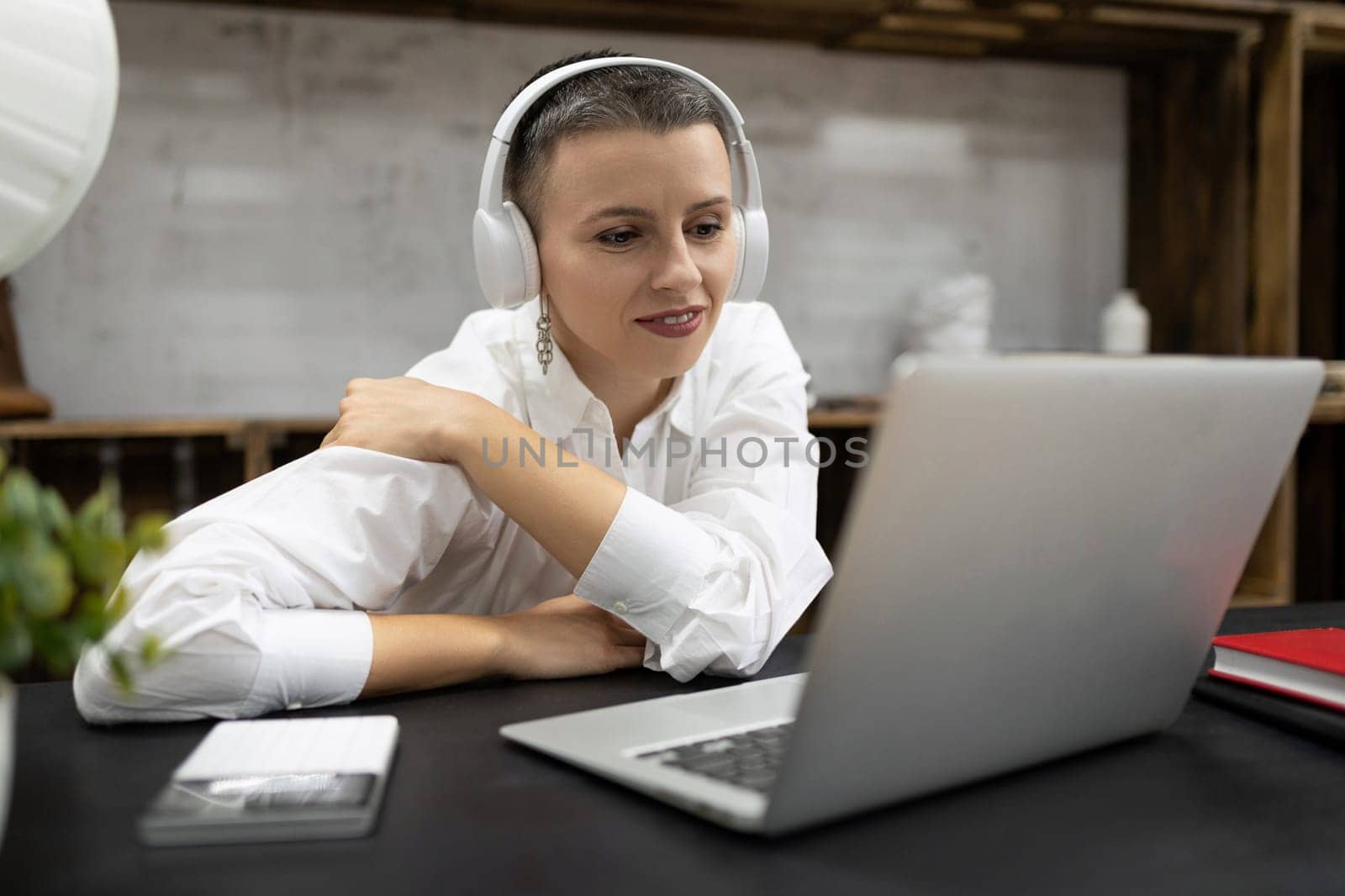 Business woman watching a webinar in headphones on a laptop while sitting at a table in the office.