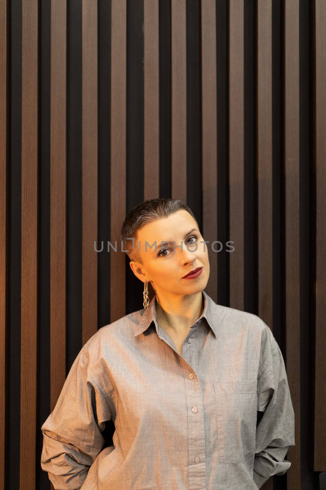portrait of a woman with a short haircut against the background of a wall with wooden vertical planks.