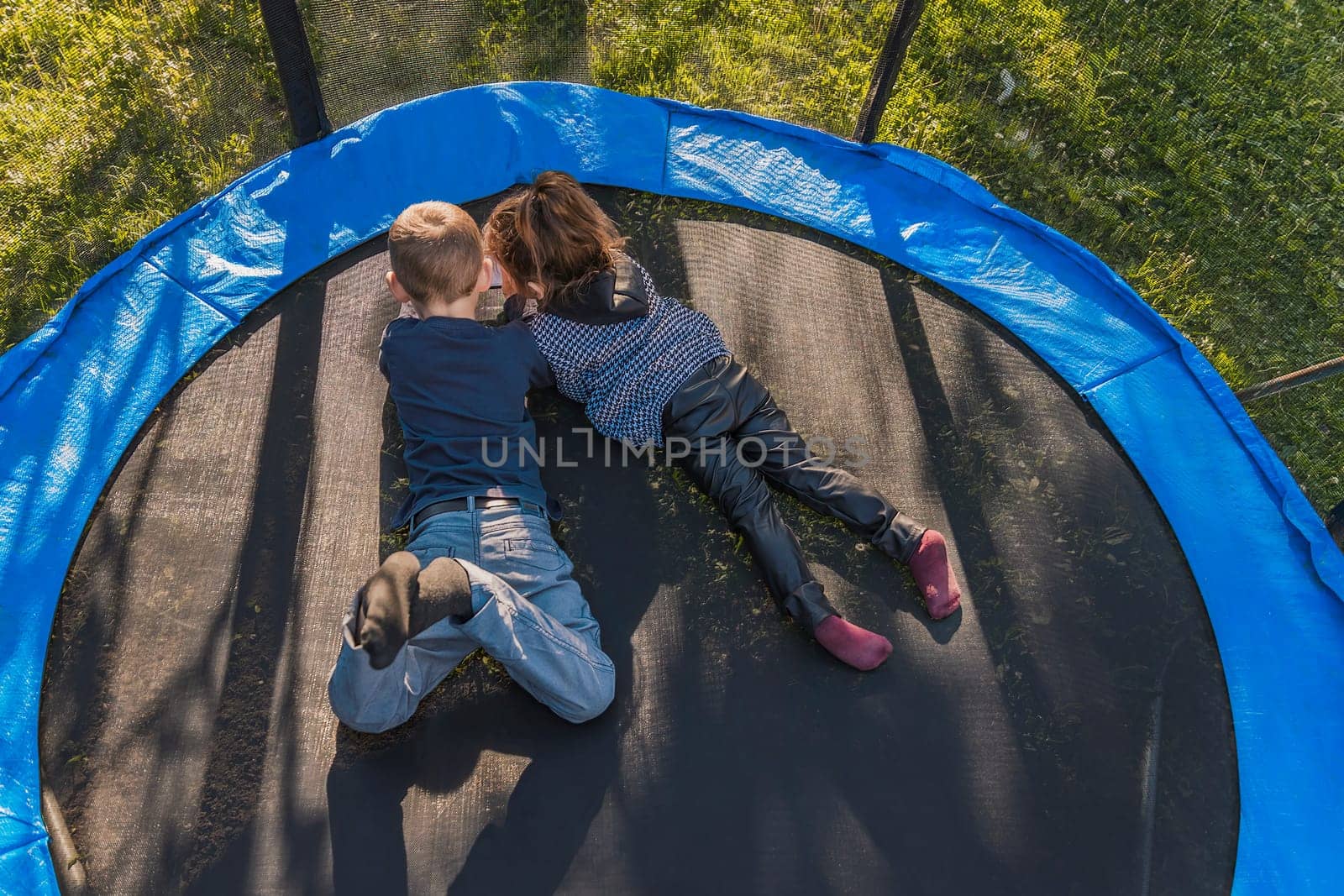 children look at the phone while lying on a trampoline, top view