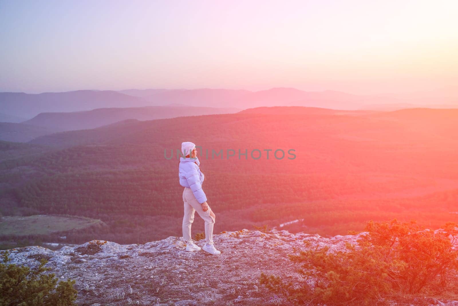 Woman tourist on top of sunrise mountain. The girl salutes the sun, wearing a blue jacket, white hat and white jeans. Conceptual design. by Matiunina