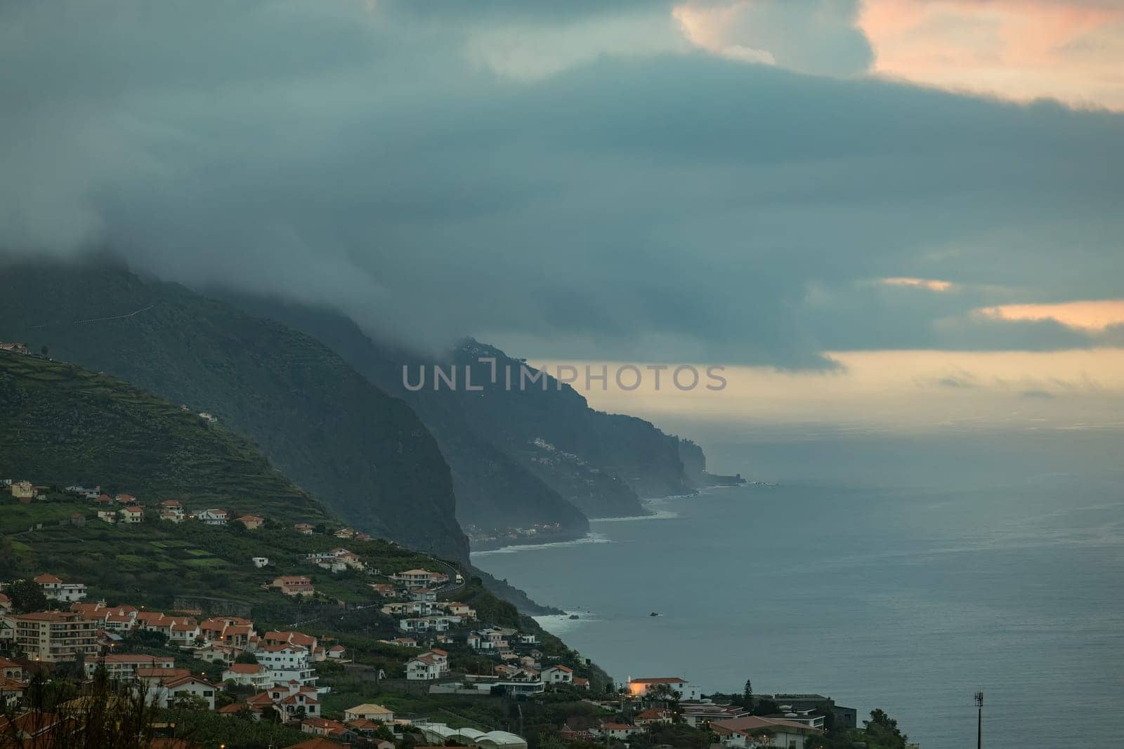 An awe-inspiring landscape of a coastal city, with its majestic mountains reaching out to the sea and surrounded by fog filled clouds. Madeira, Spain