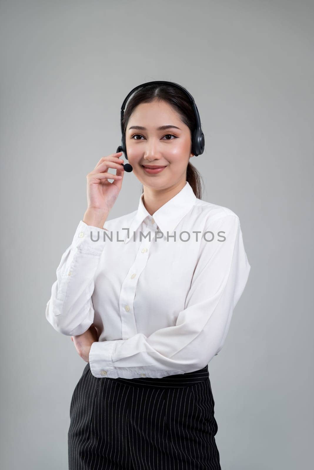 Attractive asian female call center operator with happy smile face advertises job opportunity on empty space, wearing a formal suit and headset on customizable isolated background. Enthusiastic