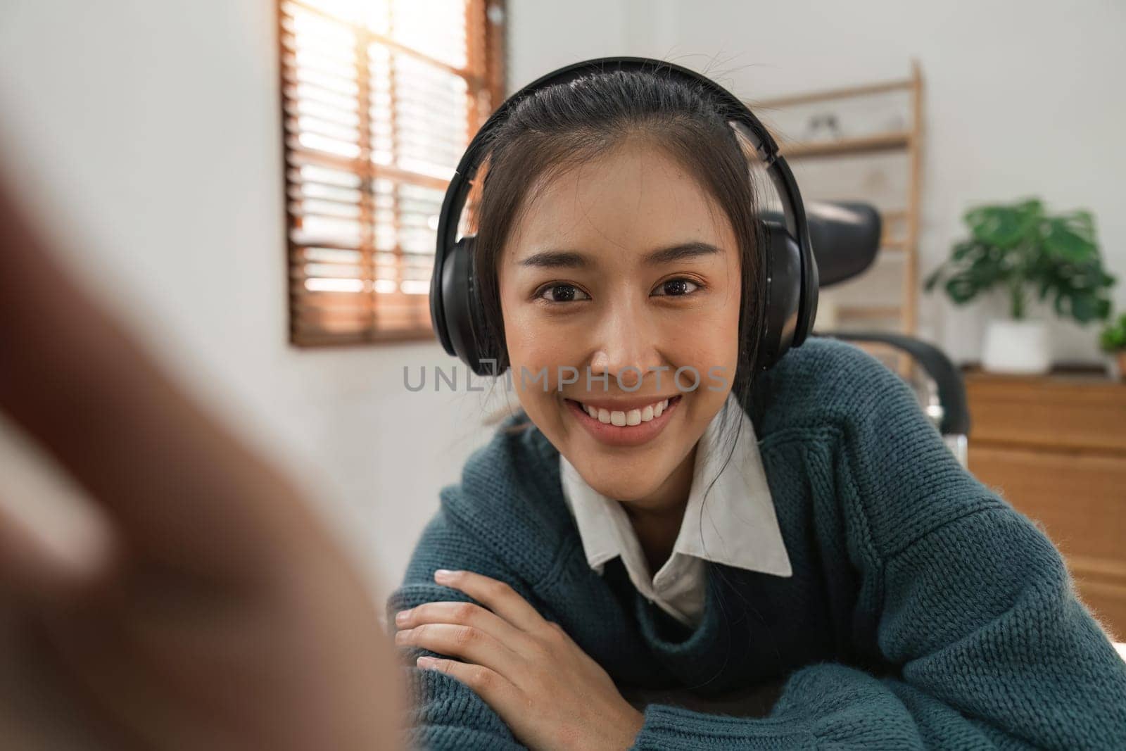 Beautiful Asian woman wearing headphone is smiling and waving to the video camera for a selfie to a friend. Online Education concept by nateemee