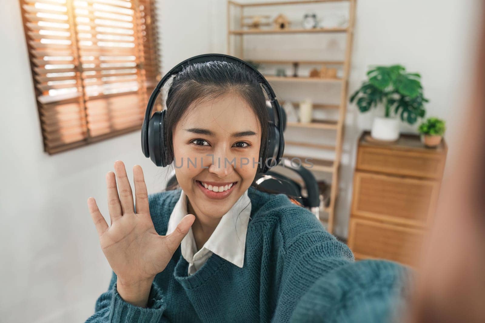 Beautiful Asian woman wearing headphone is smiling and waving to the video camera for a selfie to a friend. Online Education concept.