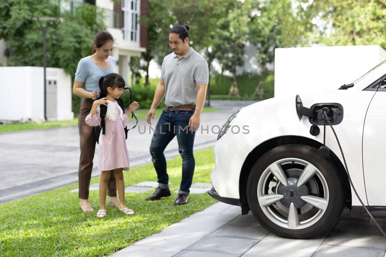 Progressive young happy family with electric vehicle and home backyard charging station. Green and clean energy from electric vehicles for healthy environment. Eco power from renewable source.