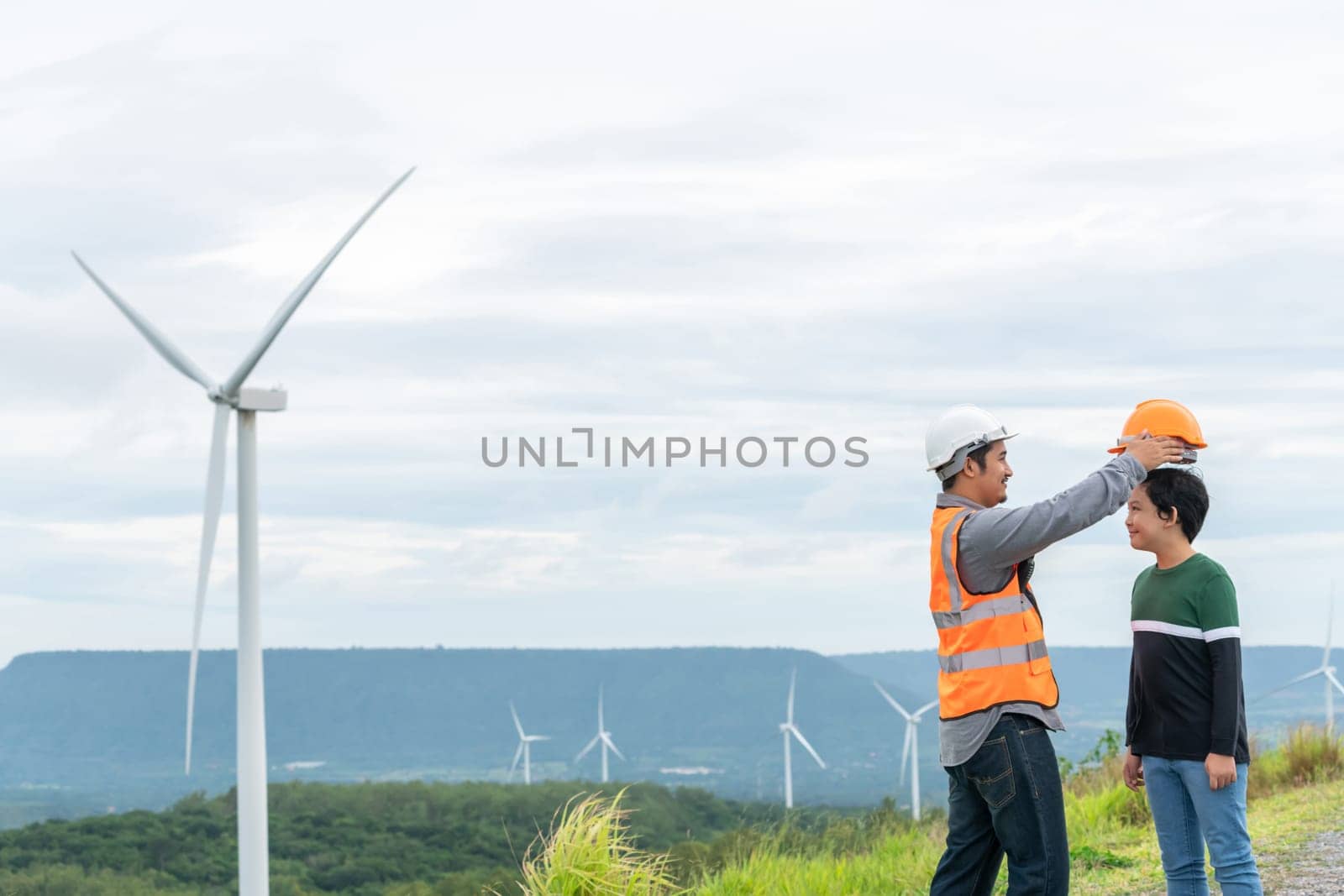 Engineer with his son on a wind farm atop a hill or mountain in the rural. Progressive ideal for the future production of renewable, sustainable energy. Energy generation from wind turbine.