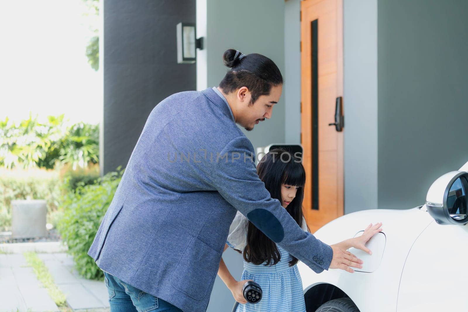 Progressive father and daughter returned from school in electric vehicle that is being charged at home. Electric vehicle driven by renewable clean energy. Home charging station concept for environment