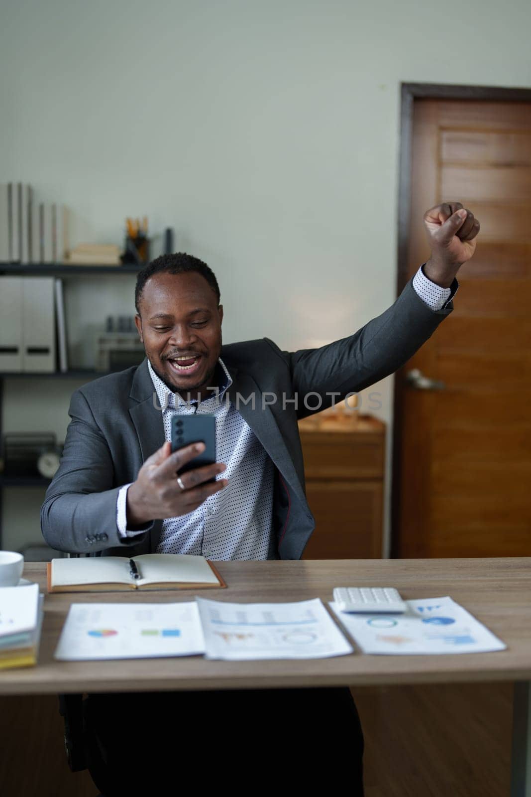 middle aged man American African business man holding smart phone mobile with hands up in winner is gesture, Happy to be successful celebrating achievement success by Manastrong