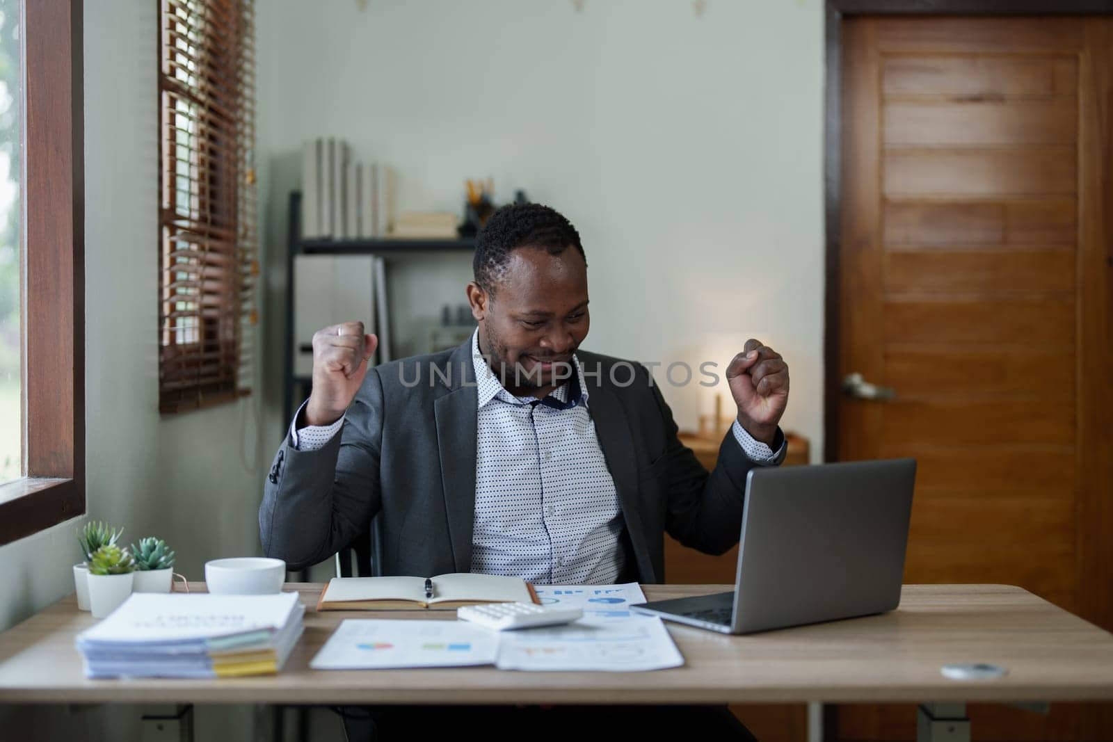 middle aged man American African business man holding computer laptop with hands up in winner is gesture, Happy to be successful celebrating achievement success by Manastrong