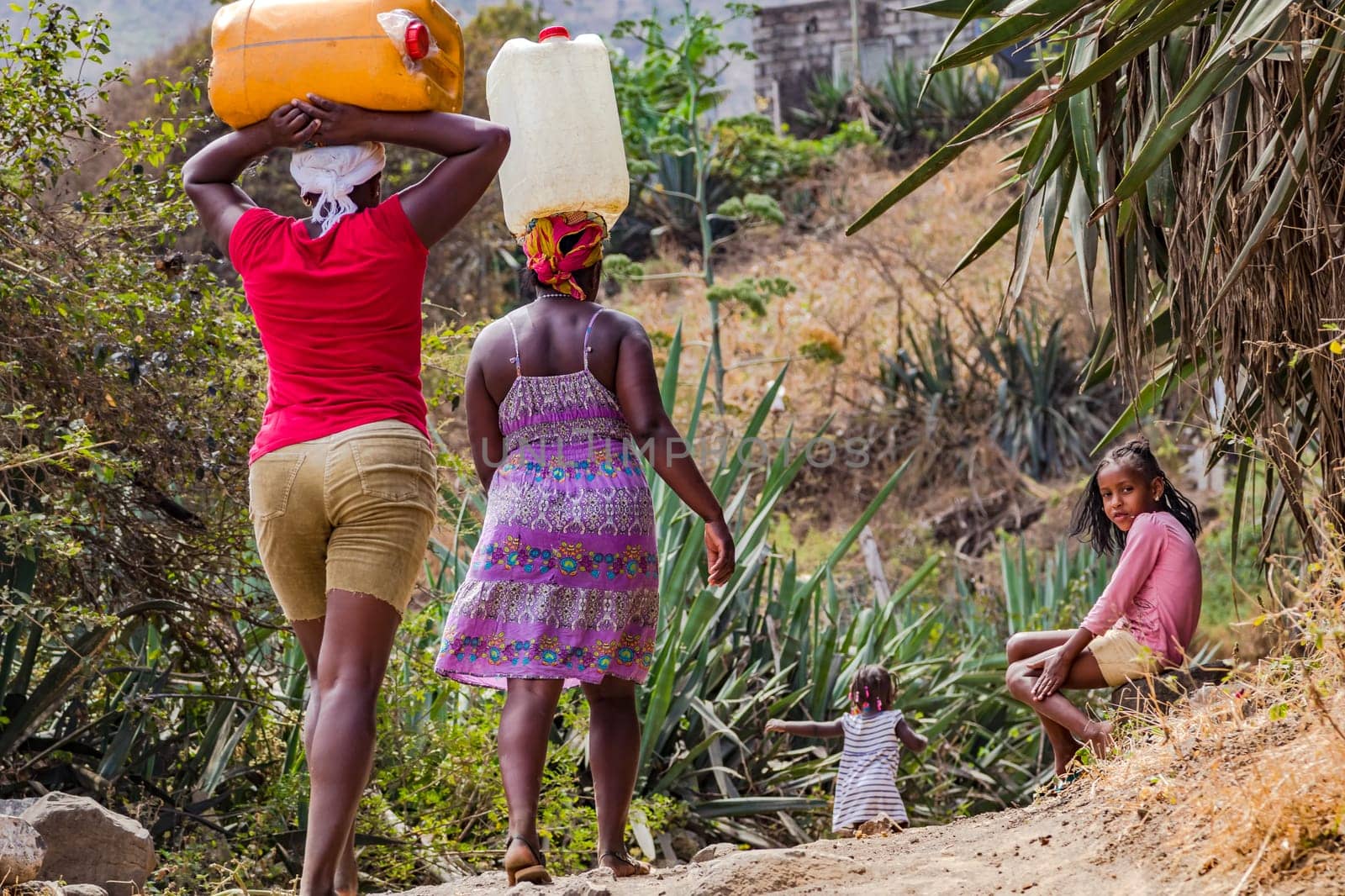 Two women and a child carrying water canisters as heavy load on their heads, Santiago Island, Cape Verde Islands