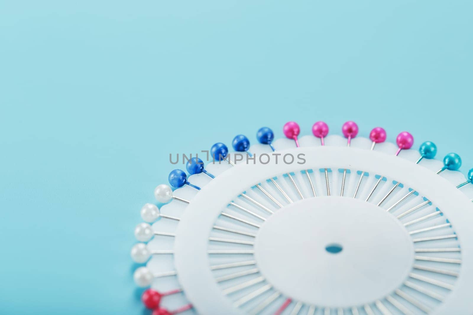 Sewing mother-of-pearl pins in a round white package on a blue background with free space