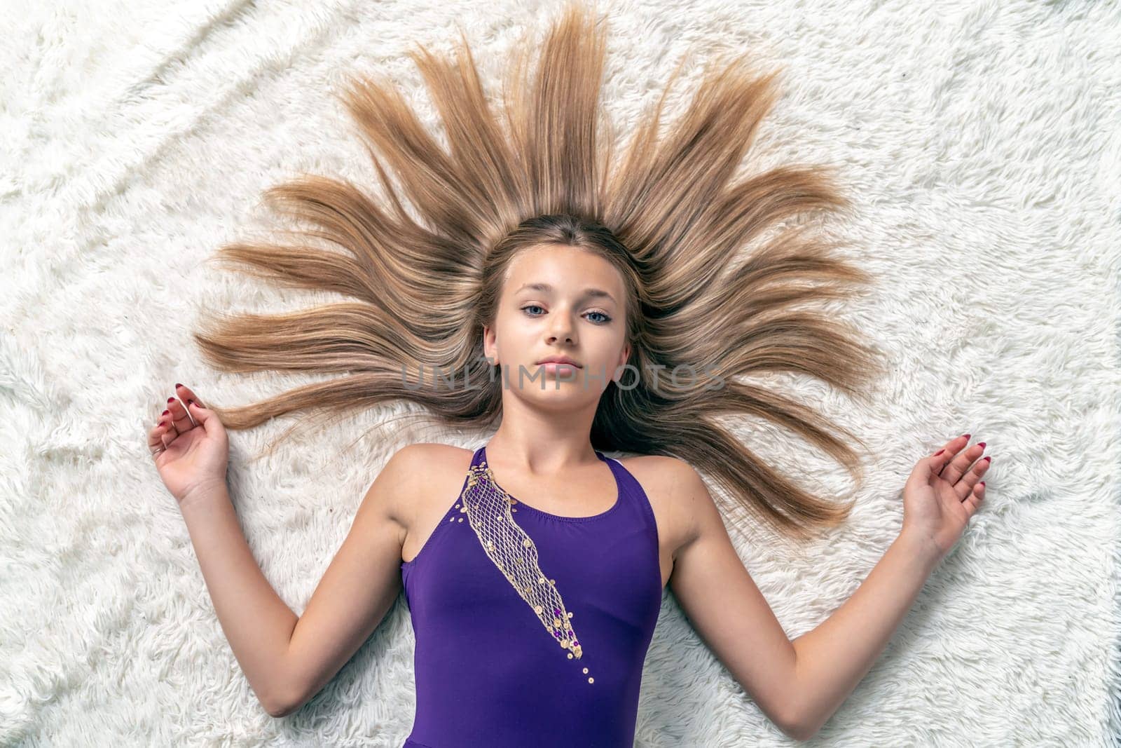 teenage girl with loose hair in the shape of the sun is lying on a white carpet. High quality photo