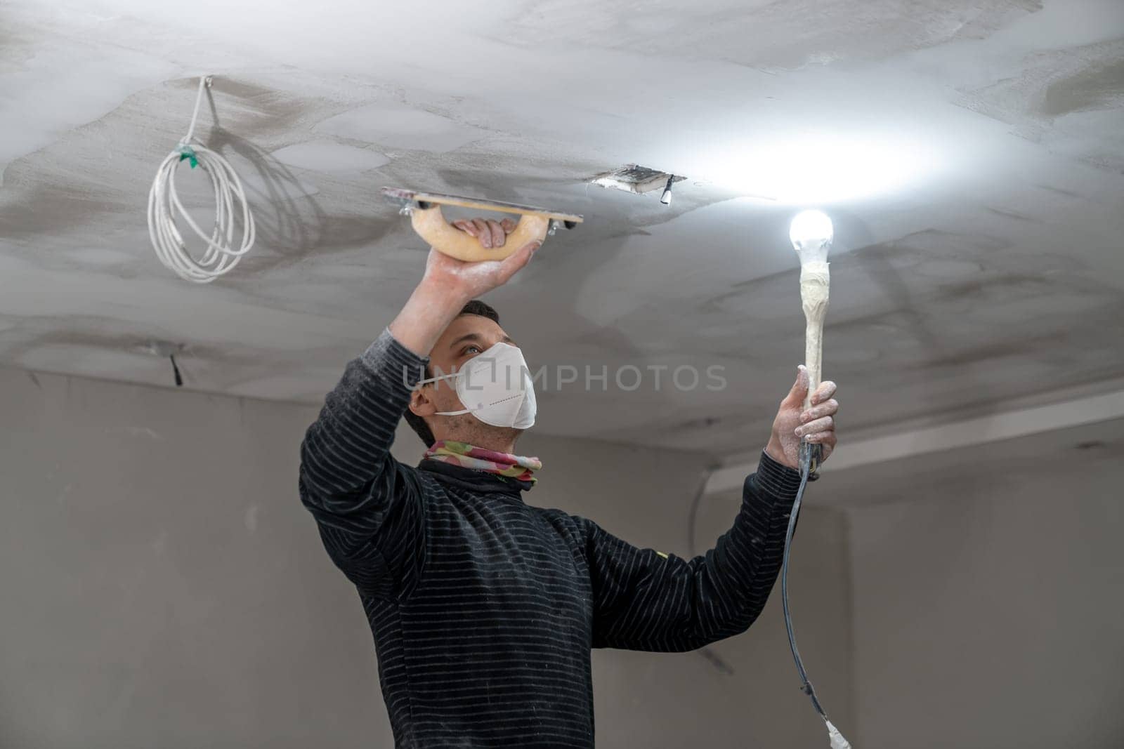 sanding a plasterboard ceiling in a new building with a trowel by Edophoto