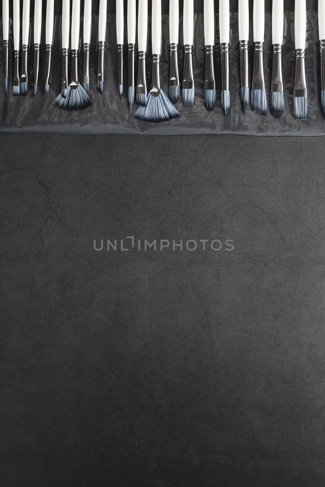 Art tools in a pencil case on a black background, top view with free space
