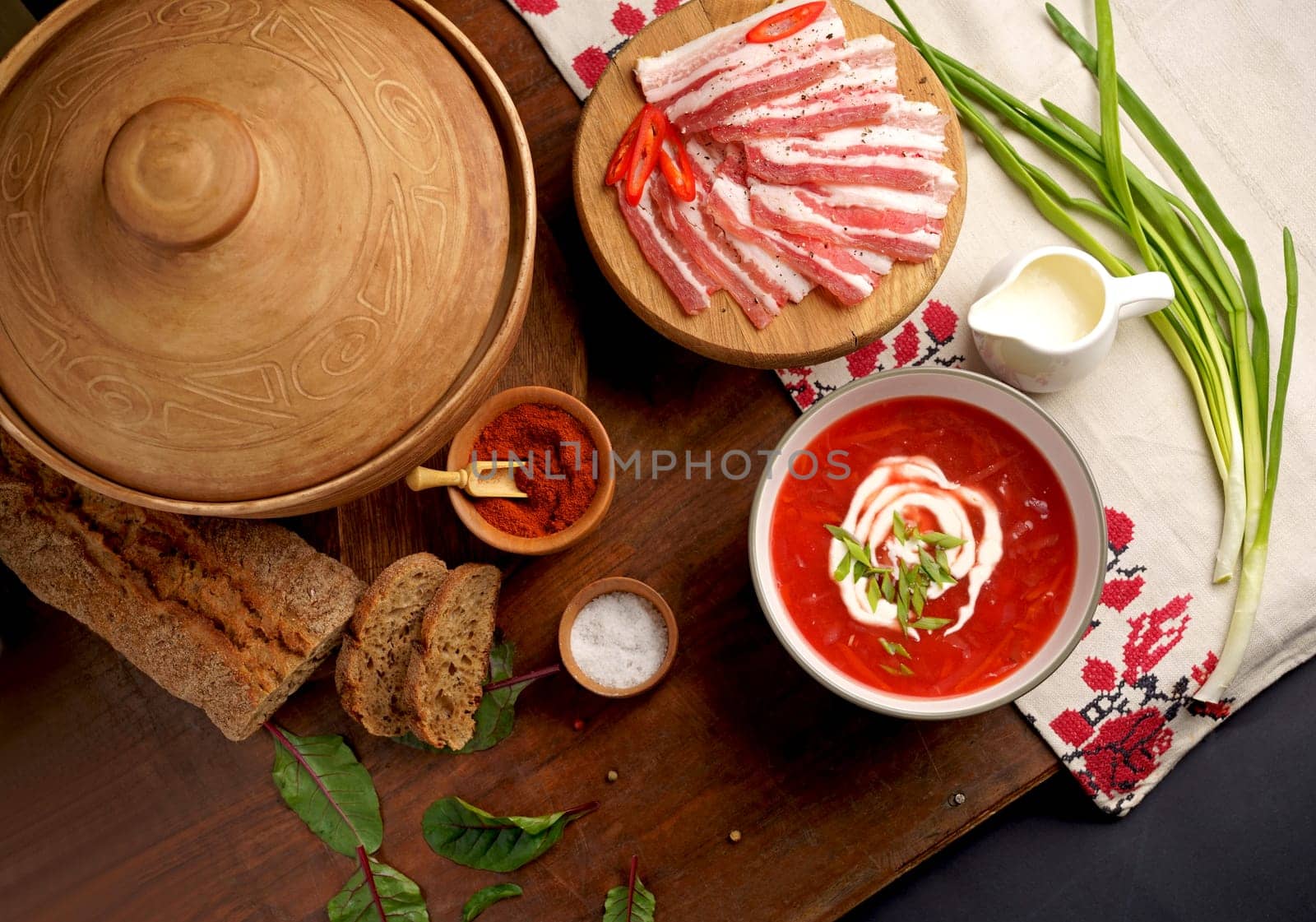 Top view of a wooden tray on a black background on which lies Ukrainian food with spices Traditional Ukrainian towel along with garlic, bread and salt. Traditional Ukrainian borsht, red vegetable soup or borscht with smetana on wooden background. Slavic dish with cabbage, beets, tomatoes. Ukrainian rushnyk. by aprilphoto