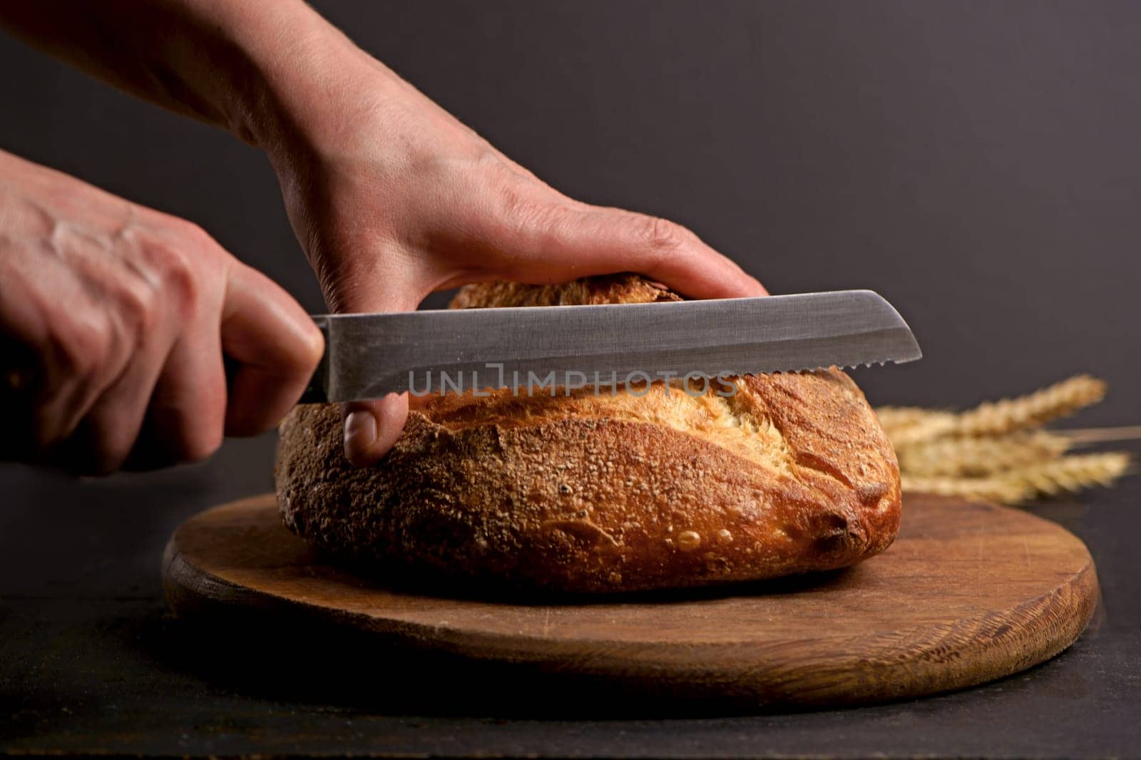 Whole grain bread put on kitchen wood plate with a chef holding knife for cut. Fresh bread on table close-up. Fresh bread on the kitchen table. The healthy eating and traditional bakery concept. Front viev.
