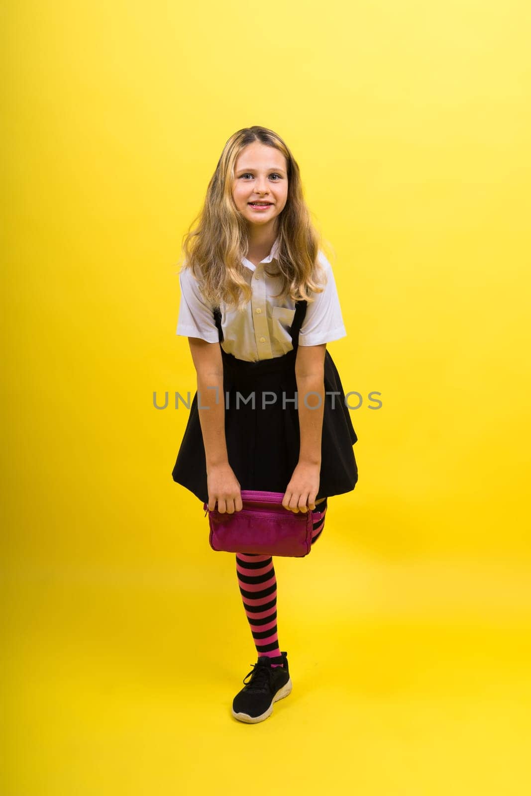 Little teenager girl with pencil case on a yellow background