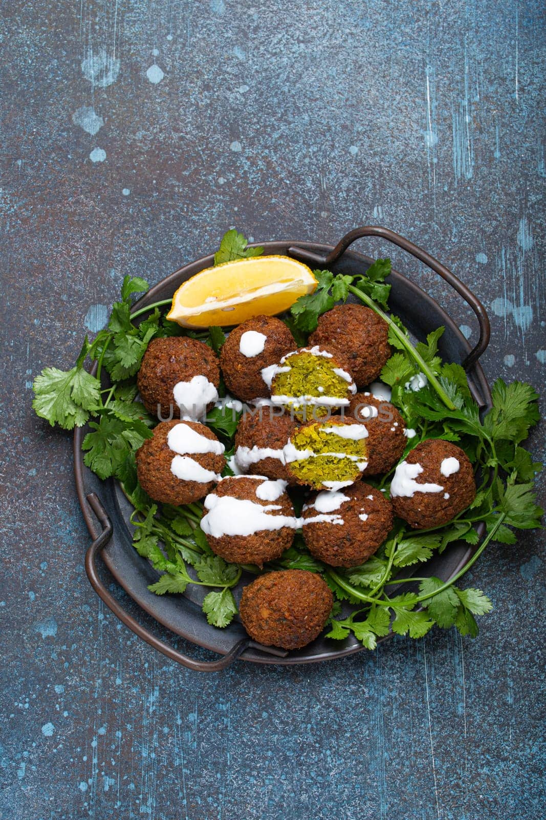 Plate of fried falafel balls served with fresh green cilantro and lemon, top view on rustic concrete background. Traditional vegan dish of Middle Eastern cuisine by its_al_dente
