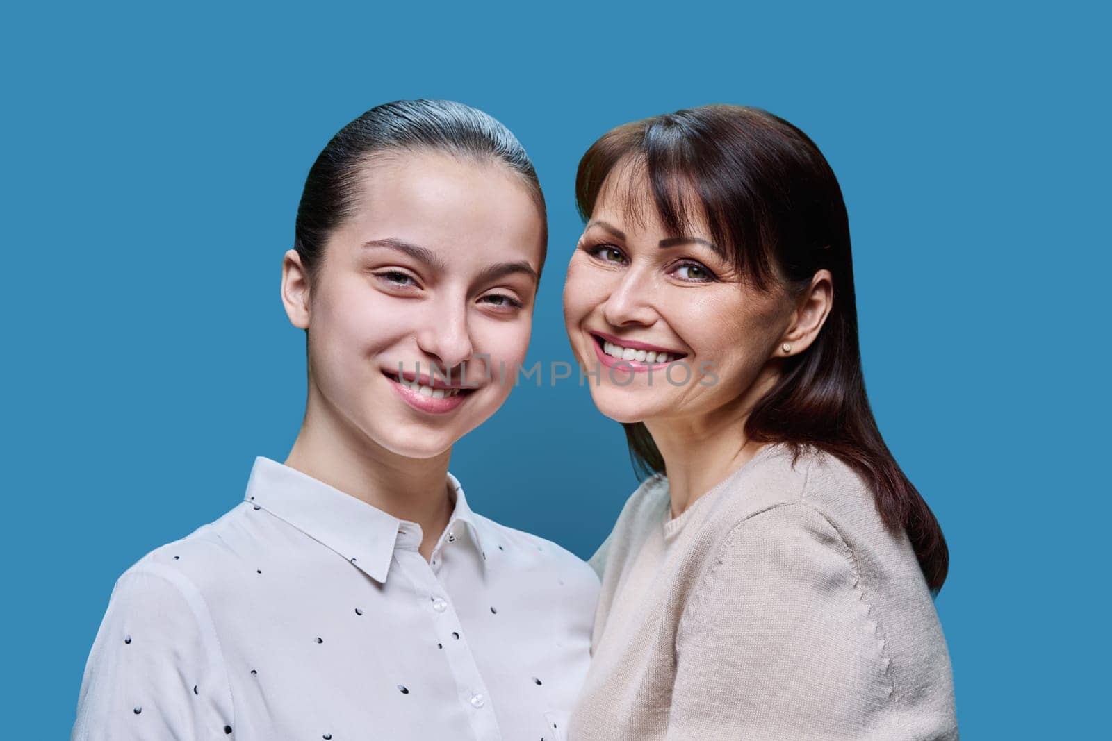 Portrait of mother and teenage daughter embracing together on blue background by VH-studio