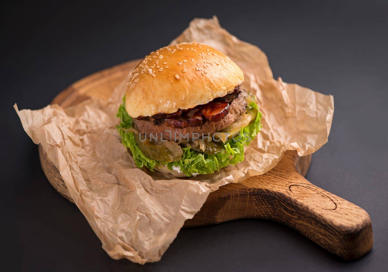 Close-up of a delicious fresh homemade burger with lettuce, cheese, onion and tomato on a rustic wooden board on a dark background by aprilphoto