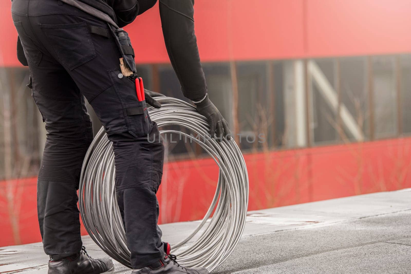 Ground wire. A worker lays a ground cable on the roof of a building. Electrician fixing aluminum wire for grounding solar panels.