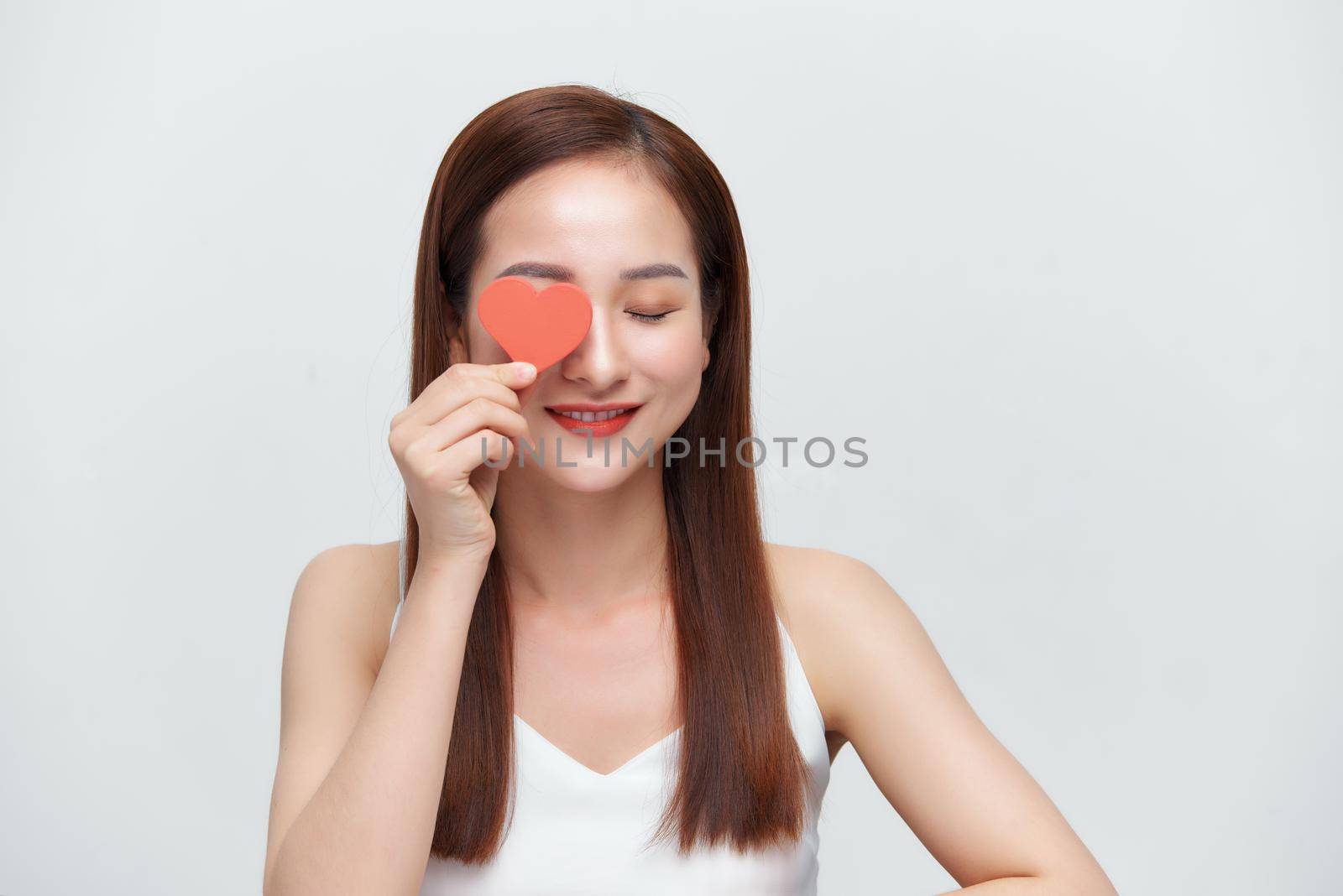 Attractive young woman holding red love hearts over eyes isolated on white background