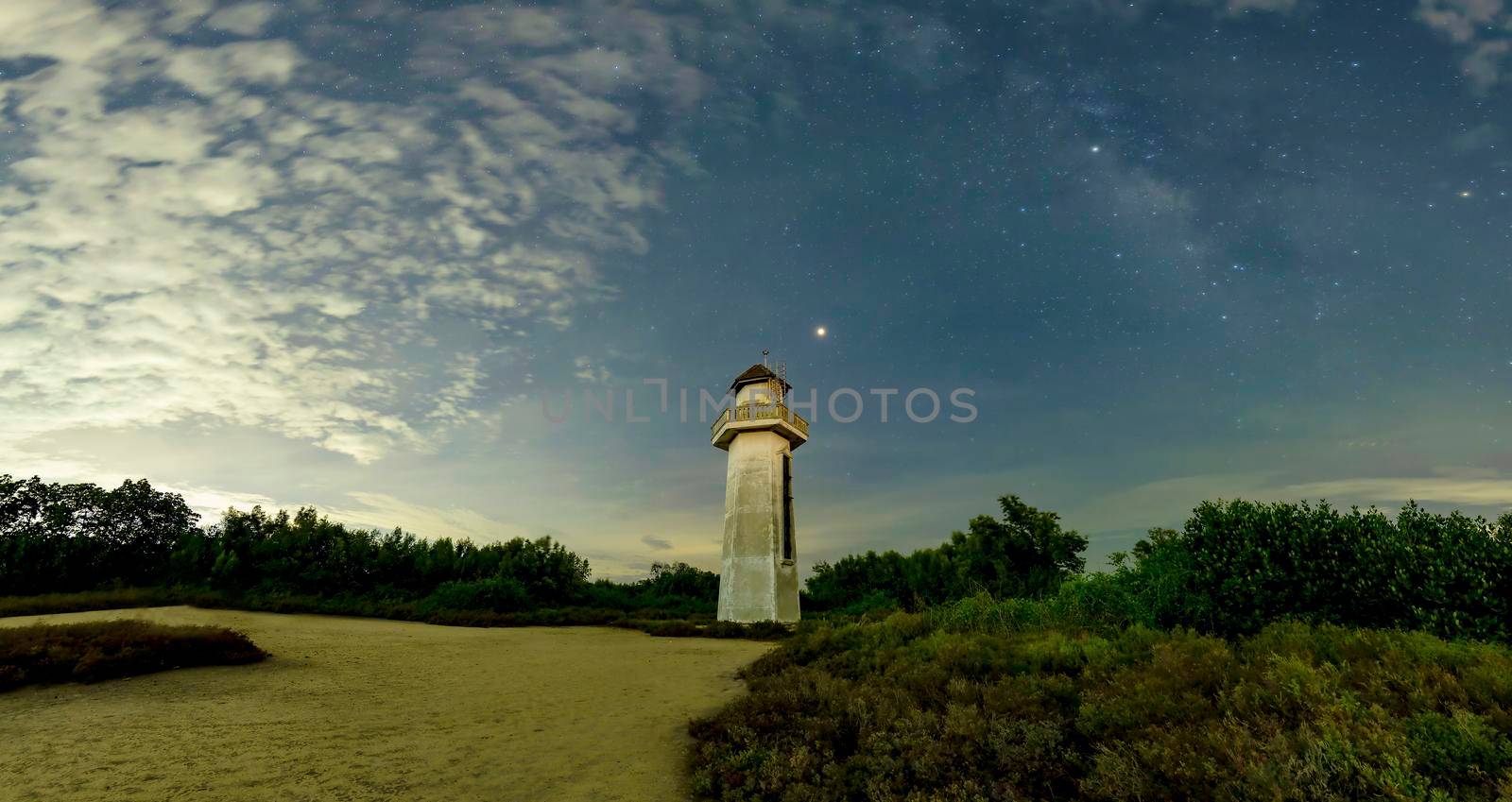 The lighthouse looks neat in the sea, the old lighthouse in the wilderness. The sky behind has clouds, stars and the Milky Way.